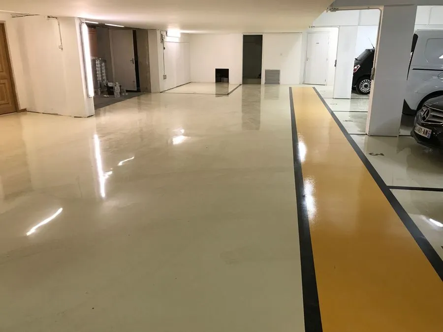 Parking couvert au sol en résine clair, allée piétonne jaune bordée de noir le long des places