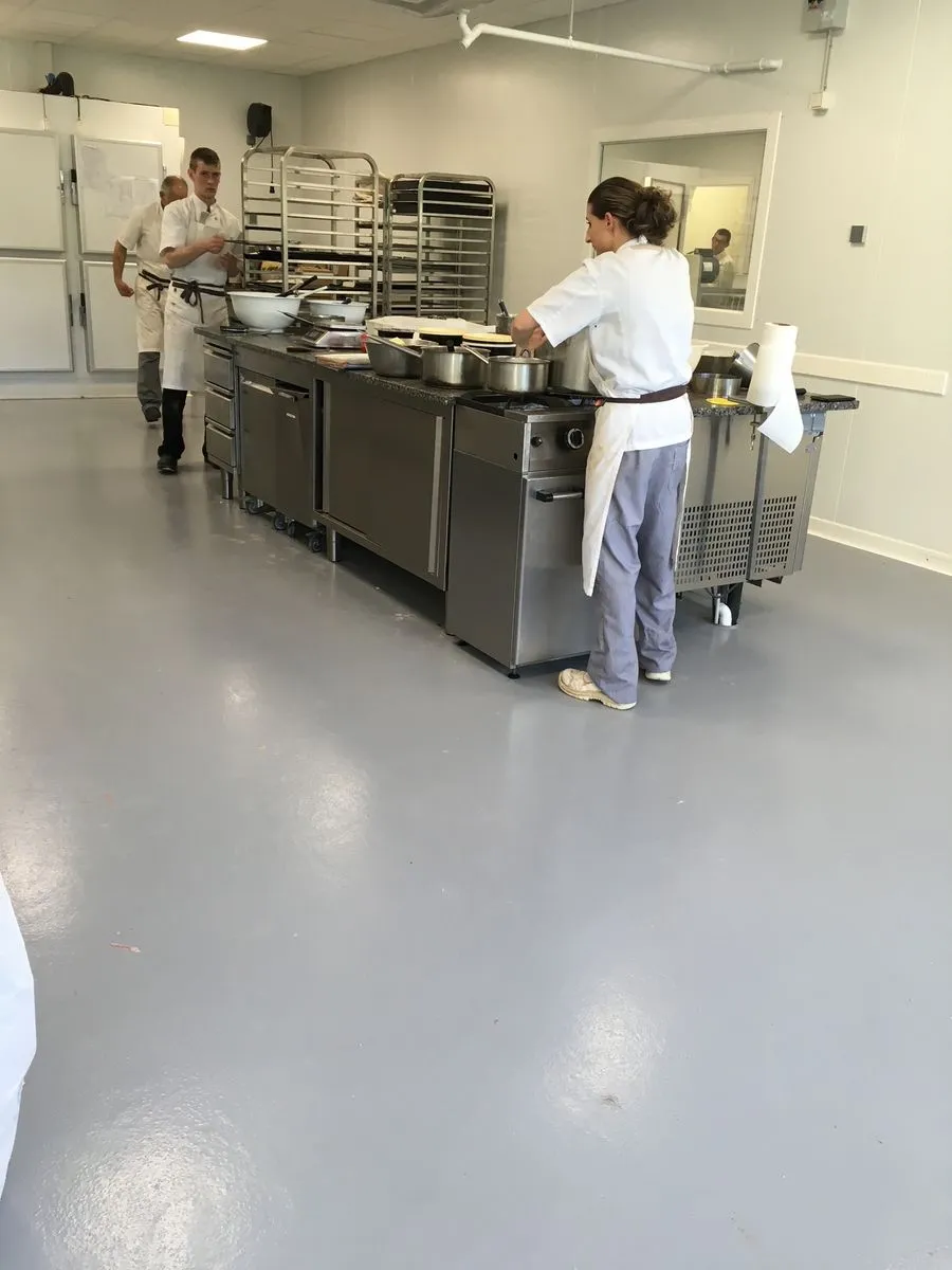 Cuisine collective au sol en résine gris, équipe au travail autour des postes de cuisson