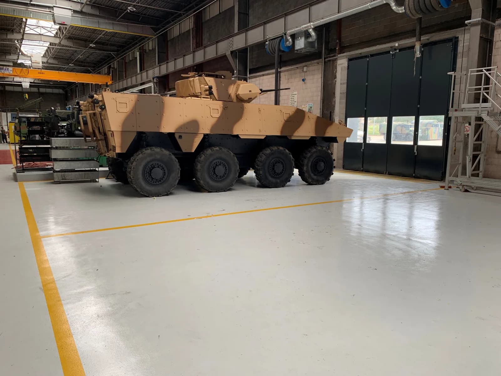 Véhicule lourd sur un sol en résine gris clair avec marquage jaune, dans un atelier de maintenance