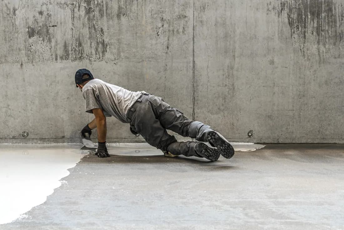 Applicateur équipé de gants et de chaussures de sécurité, raccordant un sol en résine au pied d'un mur